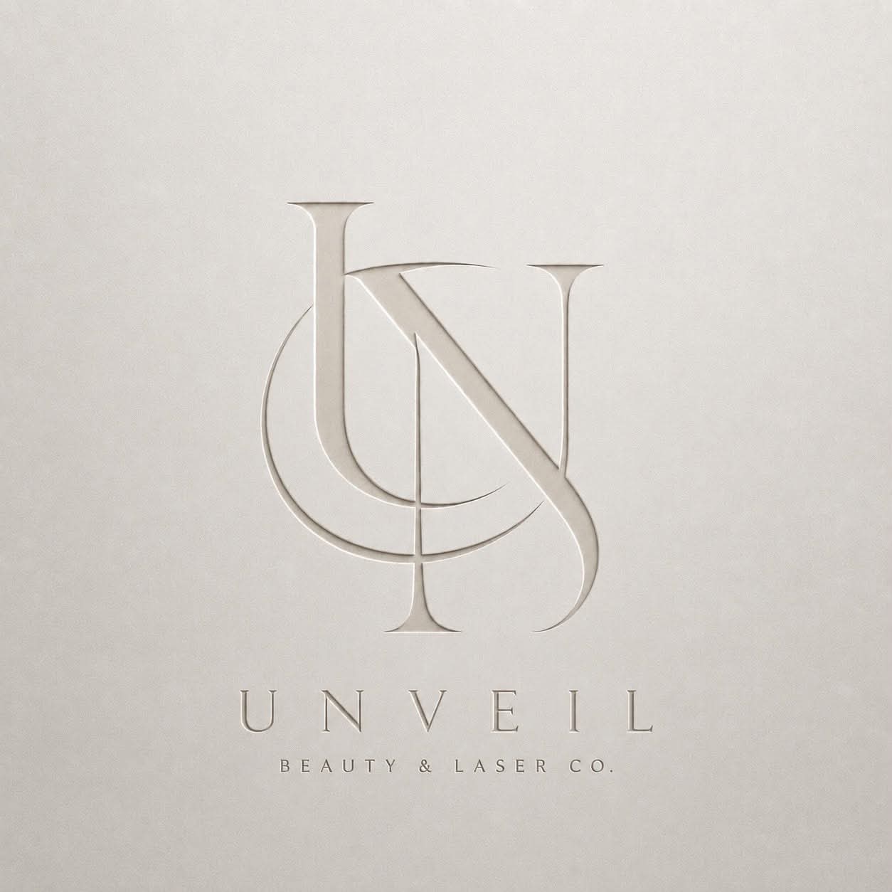 The UNVEIL monogram embossed into ivory paper, above the wordmark UNVEIL Beauty & Laser Co.